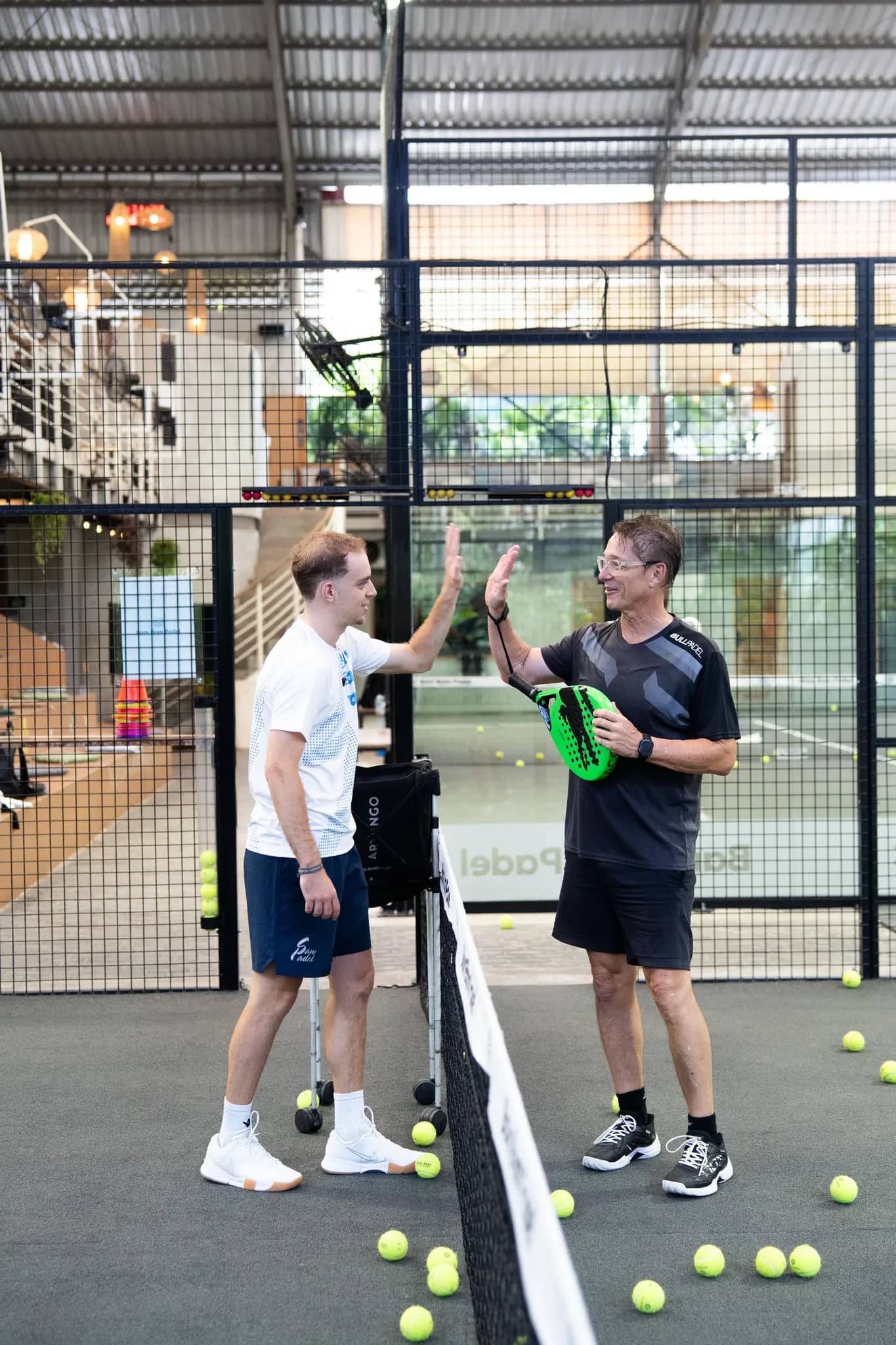 Coach Dani high-fiving a student at the net at Bam Bam Padel