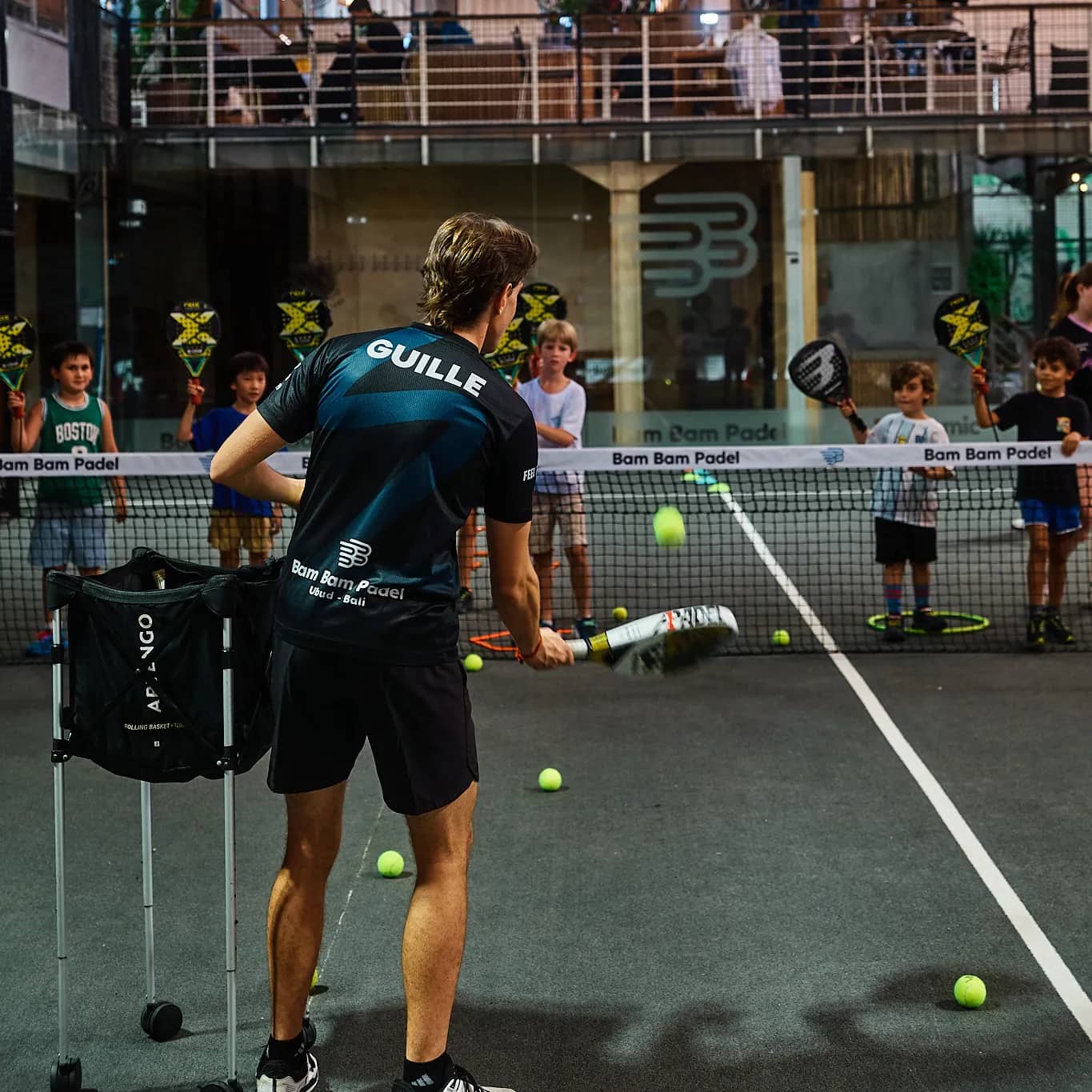 Coach Guille feeding balls to kids at the net at Bam Bam Padel