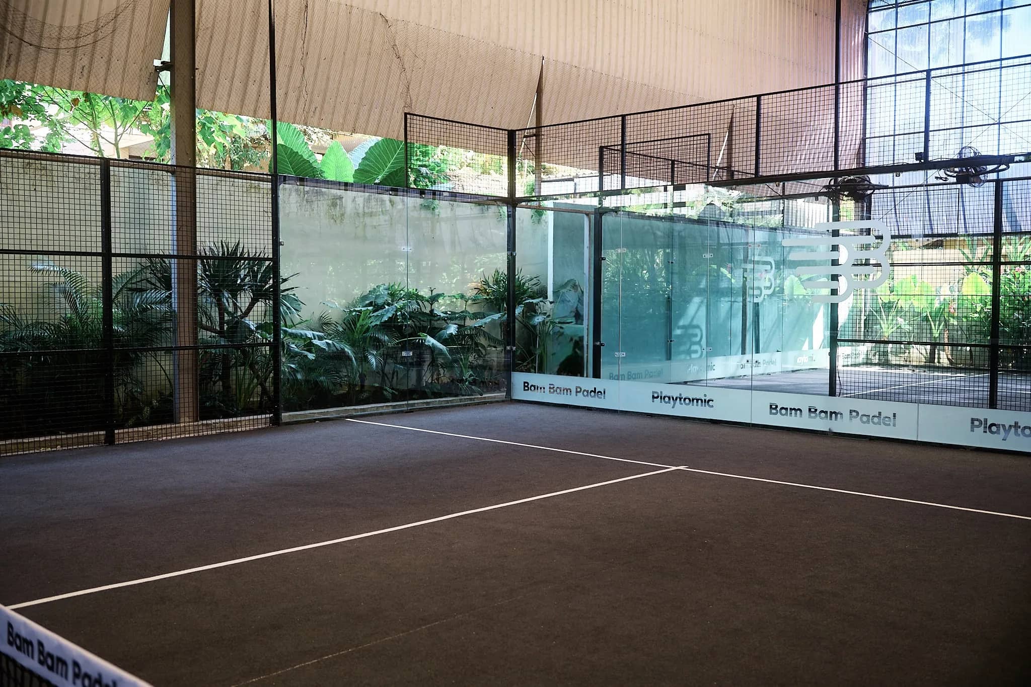 A covered court seen through the glass, greenery behind