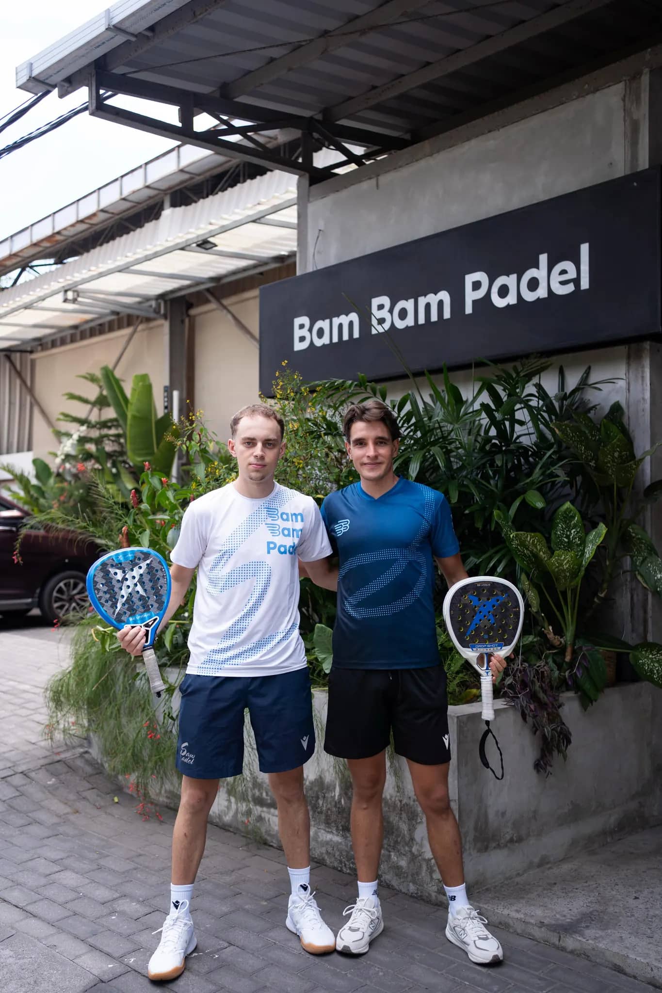 Coaches Guille and Dani standing together in front of the Bam Bam Padel sign