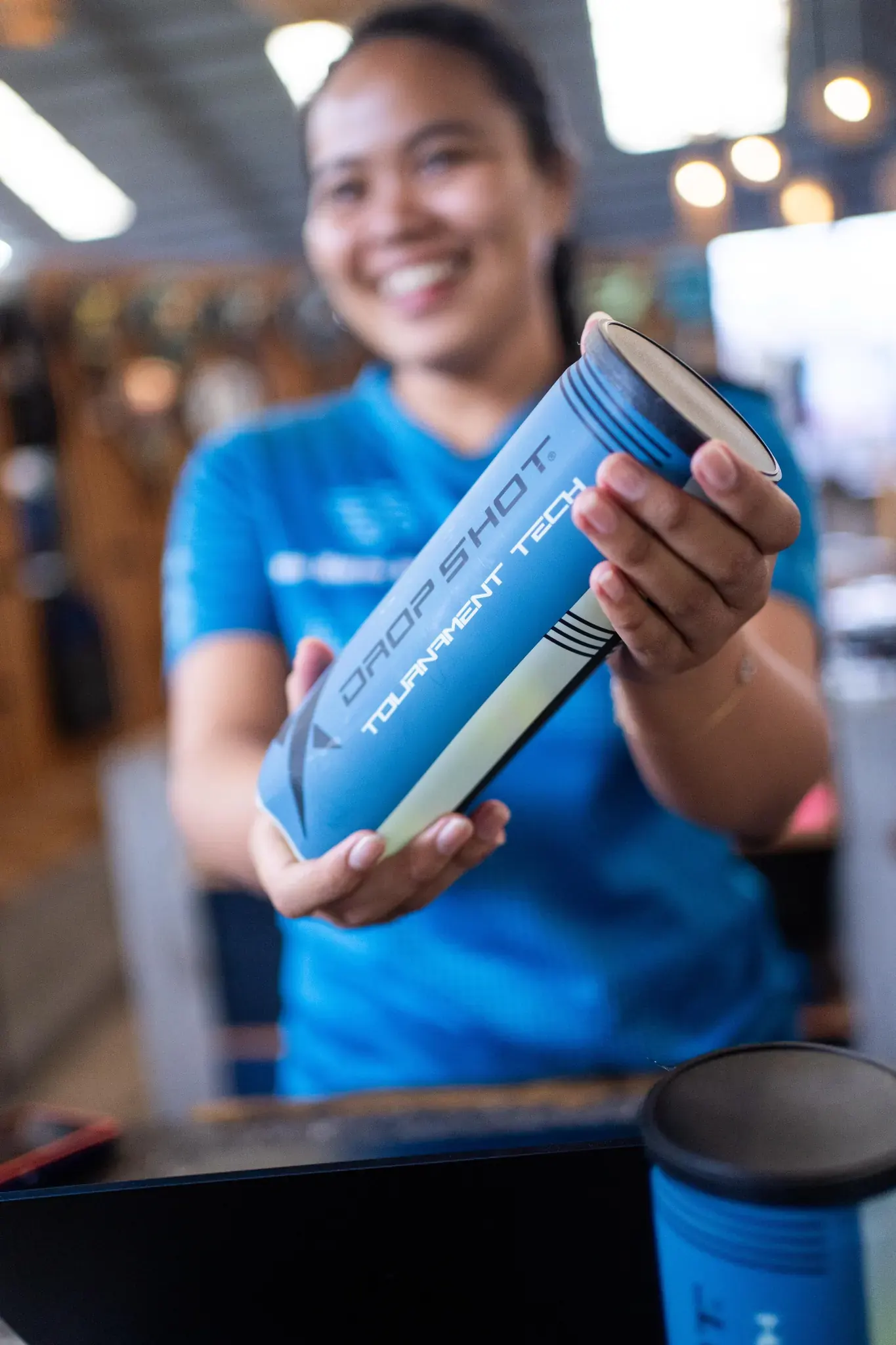 A pro-shop team member holding a Dropshot tube of padel balls