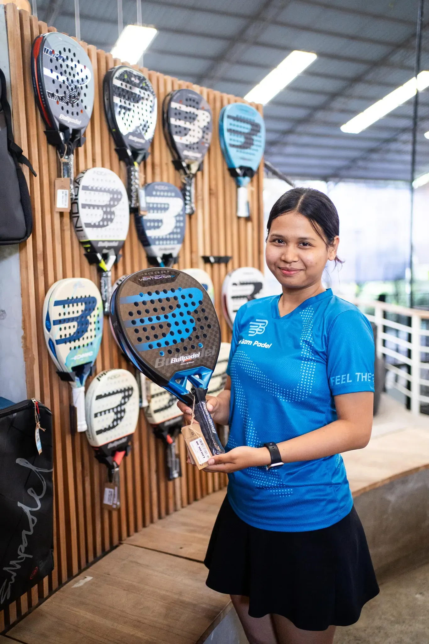 A pro-shop team member standing next to the Bullpadel racket wall