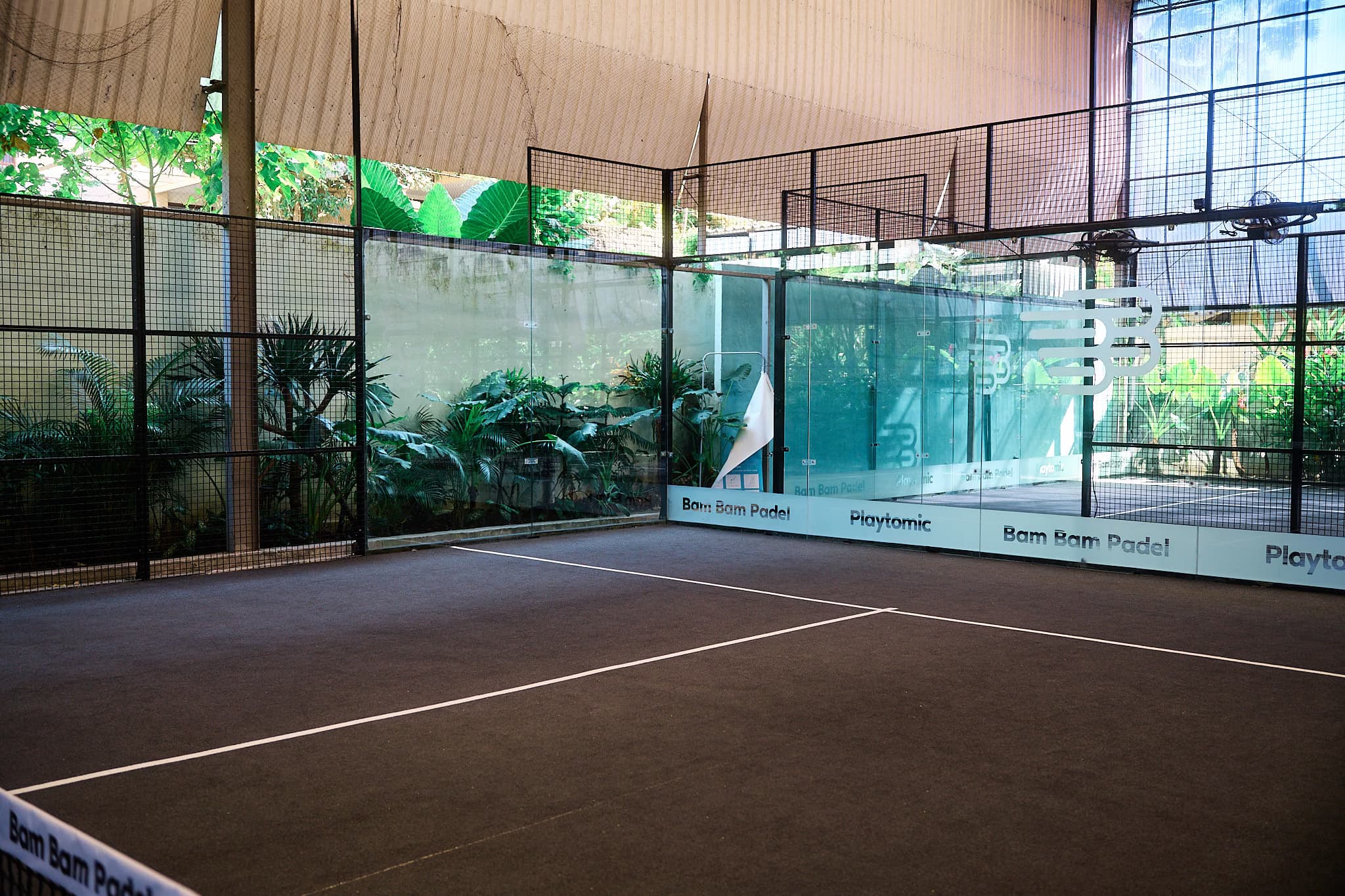 A covered court seen through the glass, greenery behind