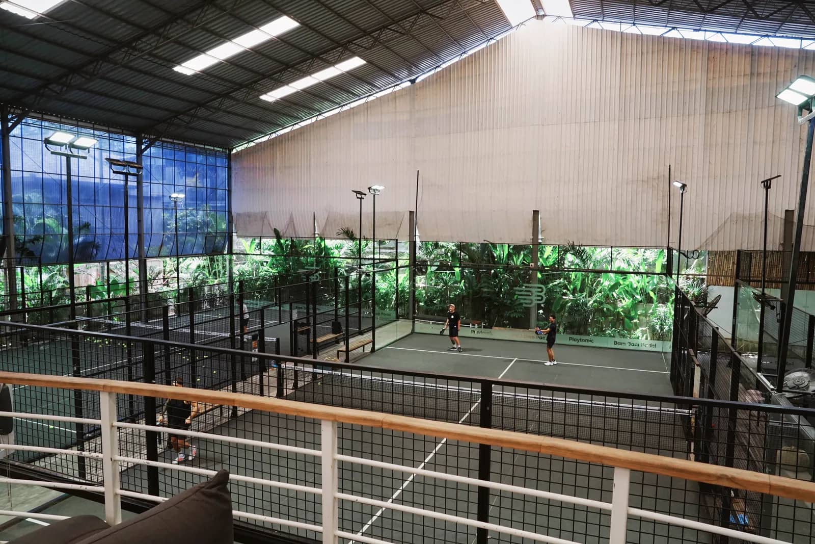 A court seen over the wooden railing, greenery behind the glass