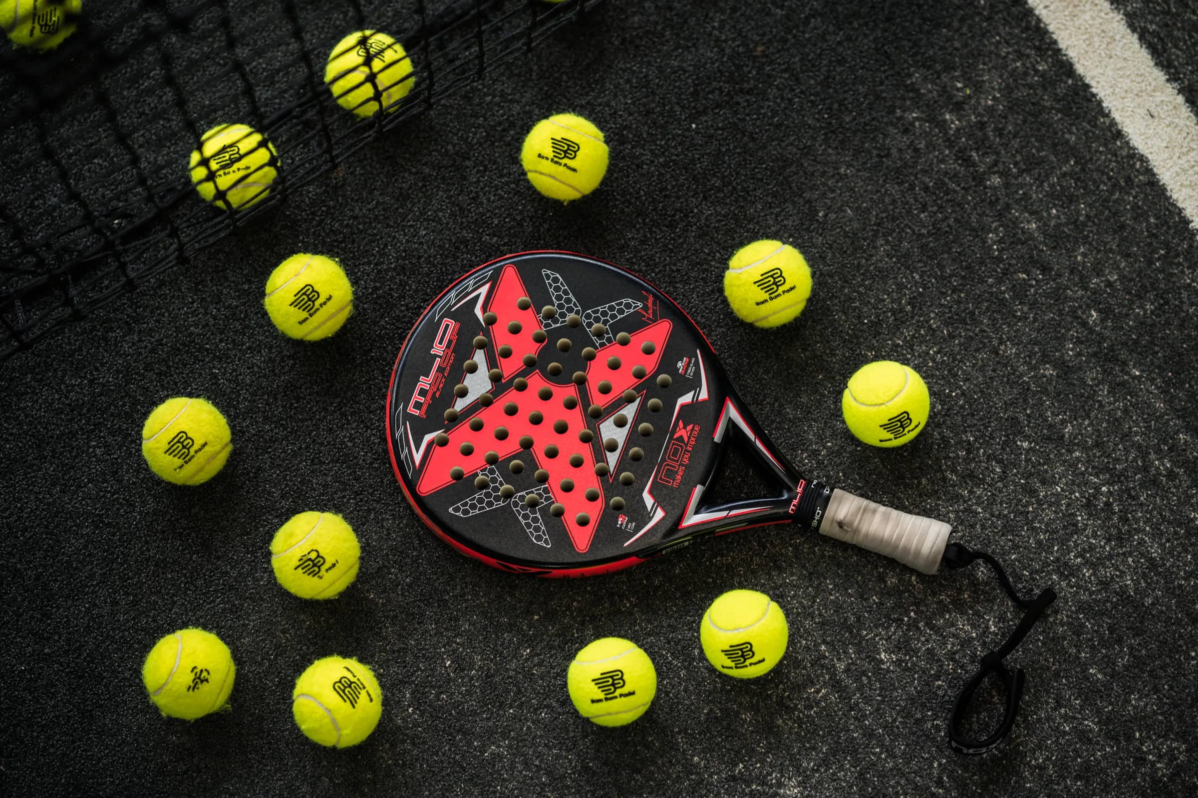 Raket padel dikelilingi bola Bam Bam Padel di lapangan